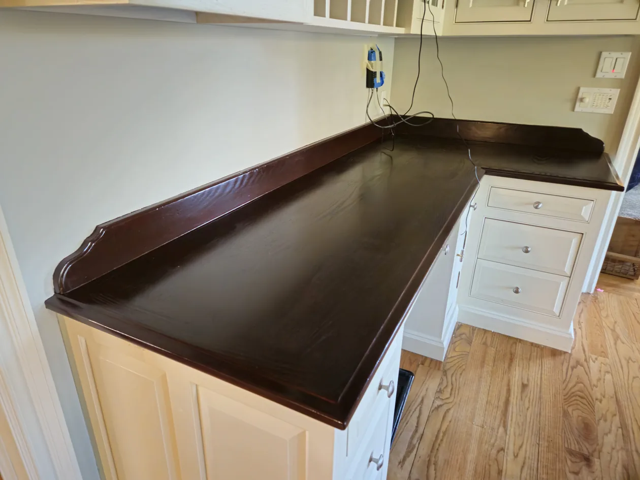Dark kitchen countertop beside light cabinets, with small items near the edges.