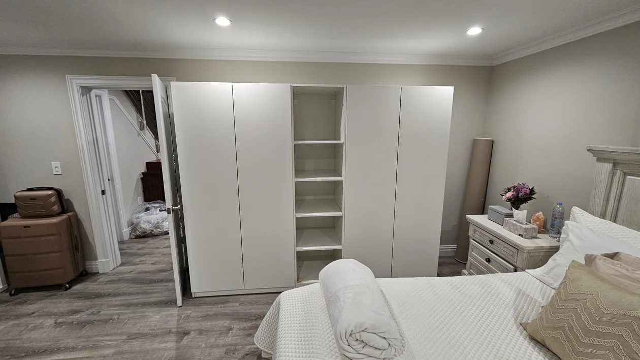 Tall white wardrobes and open shelving in a bedroom.