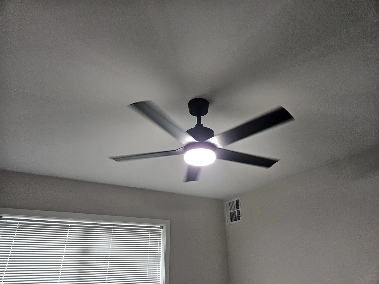 Dark ceiling fan with a central light in a bedroom.