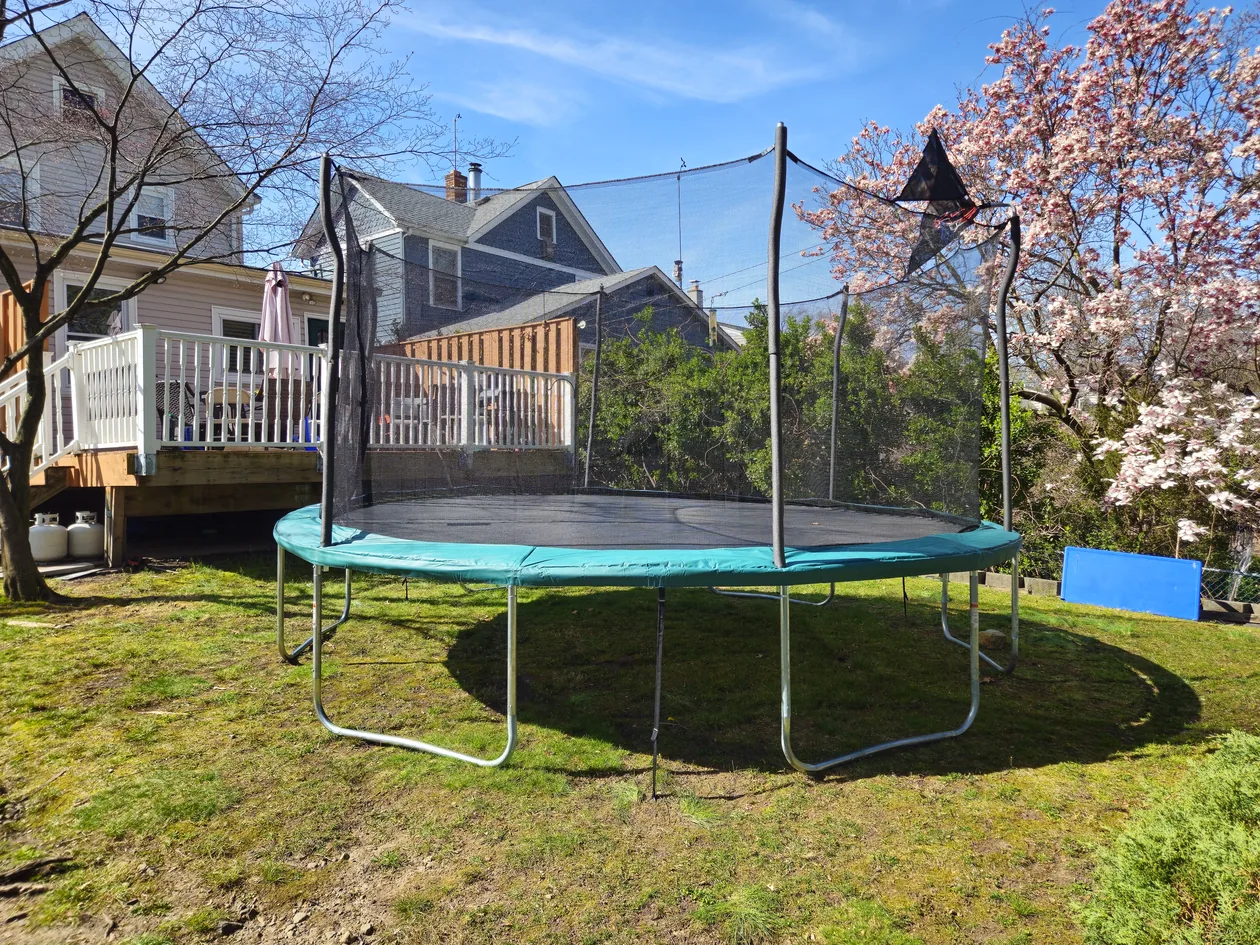 Trampoline on a lawn beside a deck and garden.