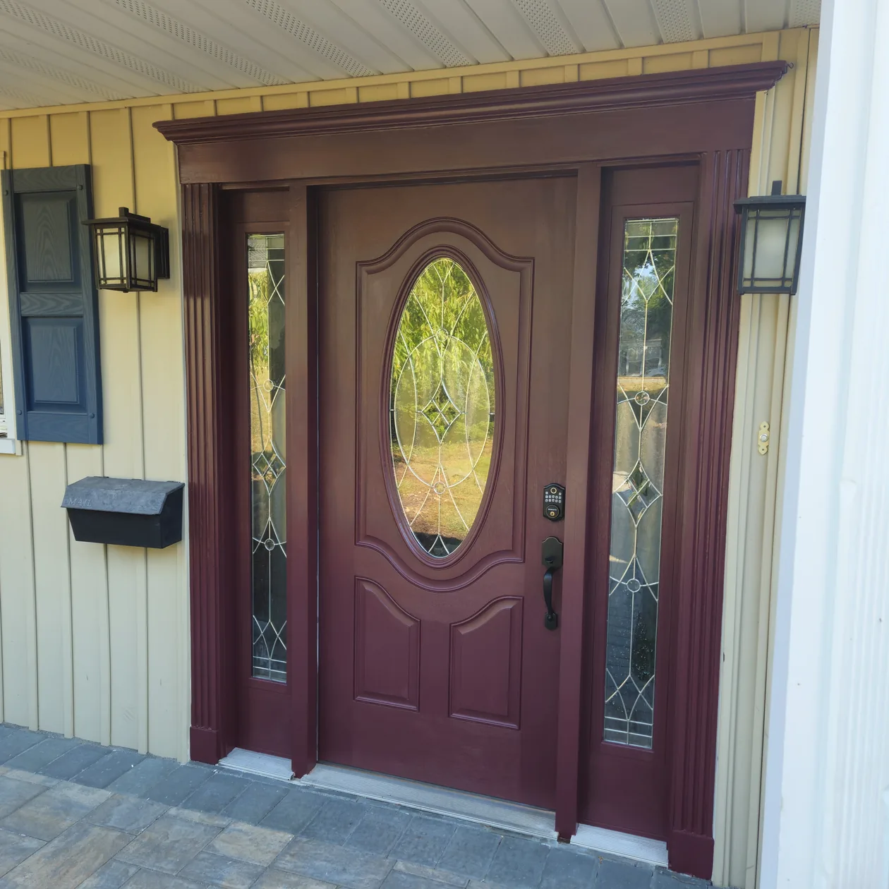 Dark decorative entry door with oval glass and matching sidelights.