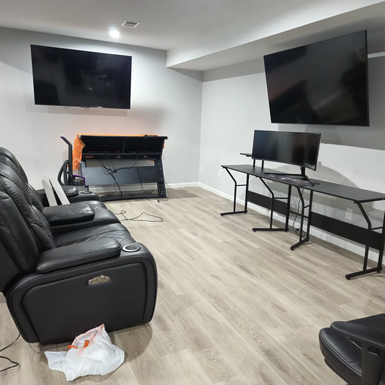 Two televisions mounted on a living-room wall above seating and a media stand.