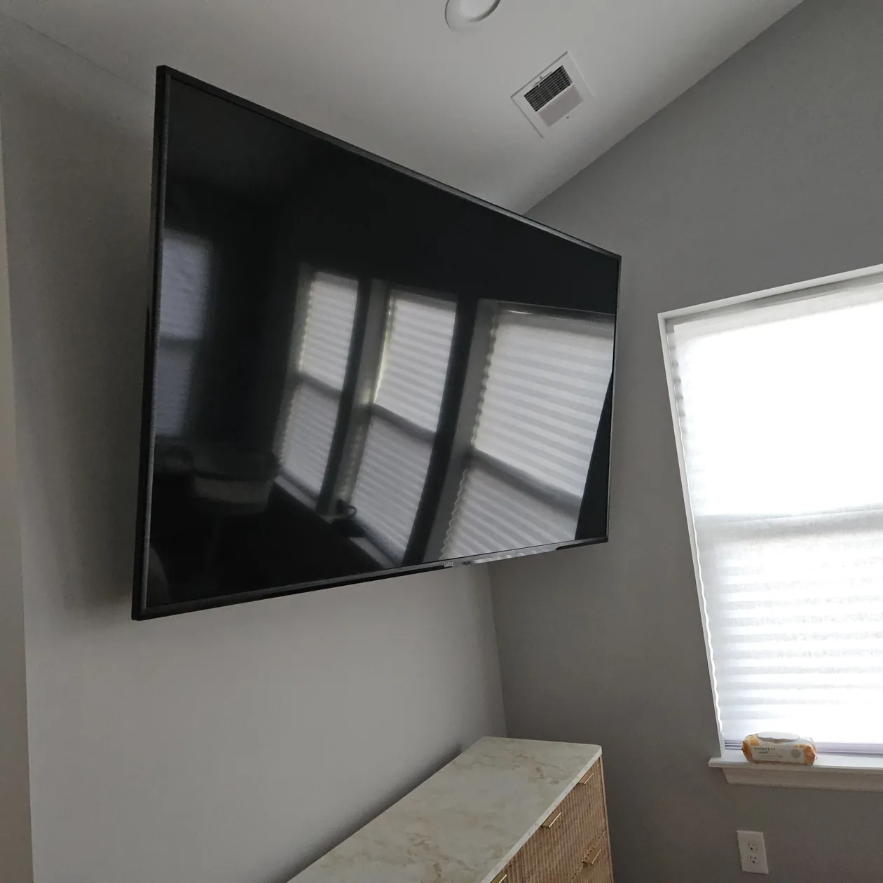 Large wall-mounted television on a gray wall near a window.