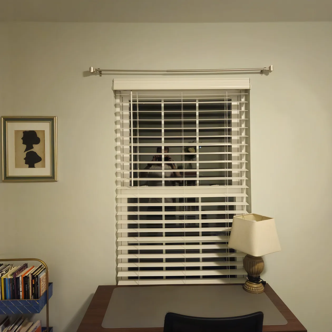 White window blinds above a desk and table lamp.