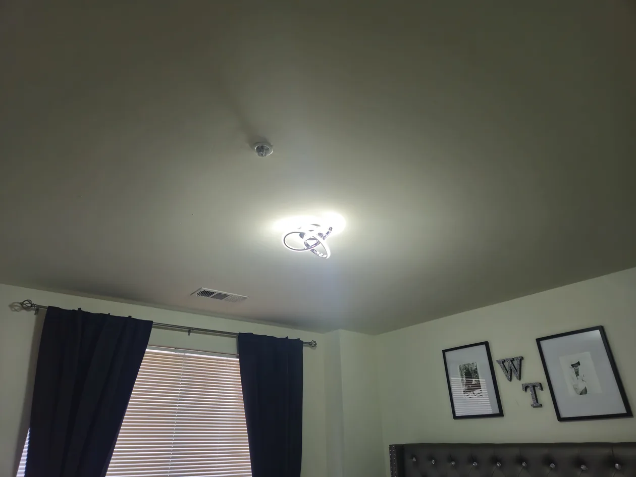 Small illuminated ceiling light in a bedroom with a window and wall art.