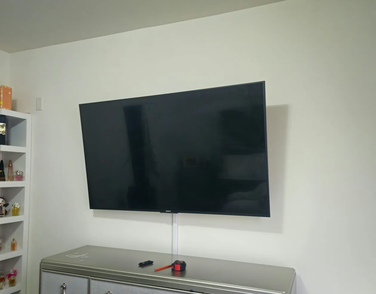 Wall-mounted television above a dresser in a bright room.