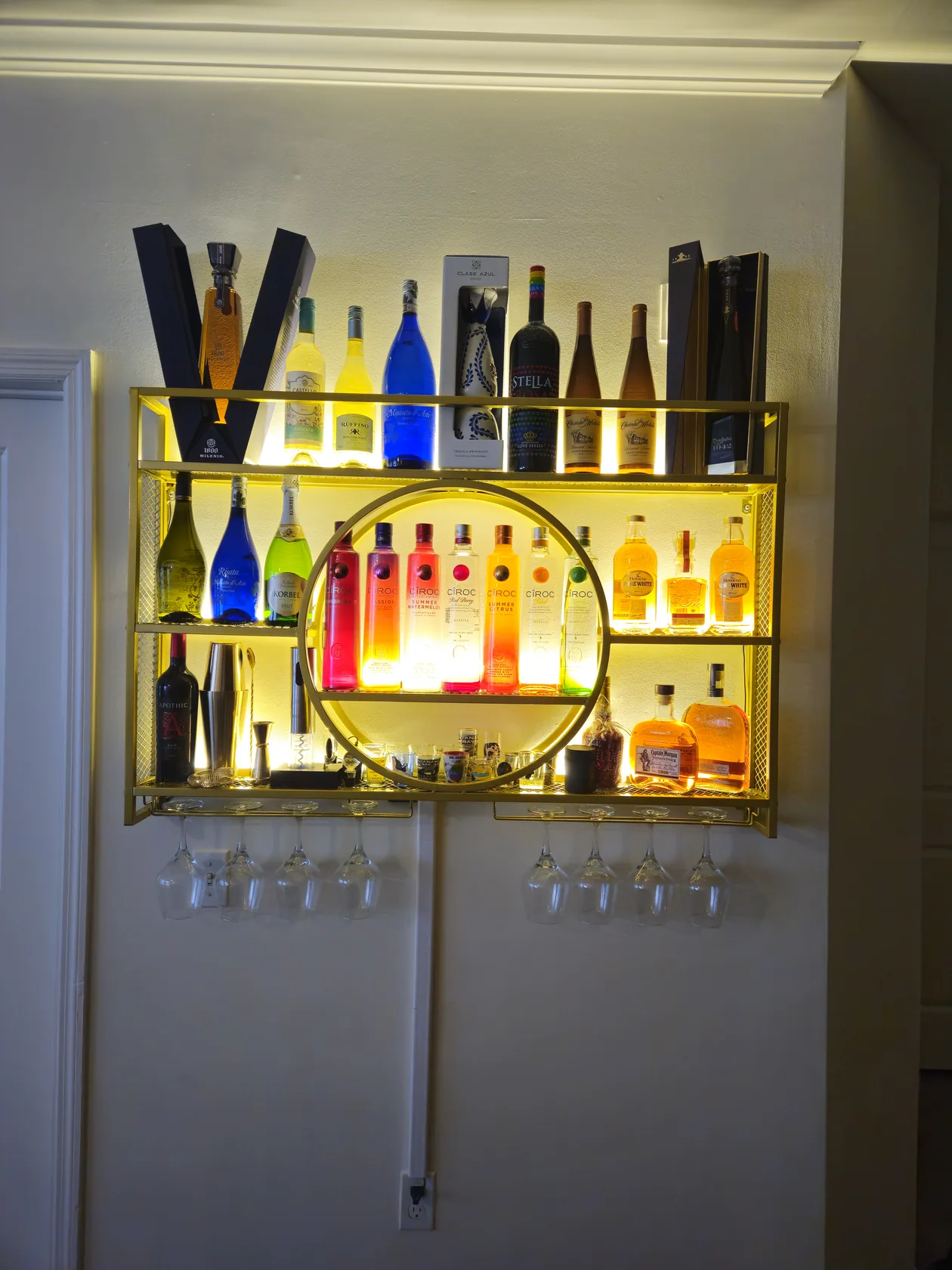 Bottle shelves and glassware in a lit wall niche.