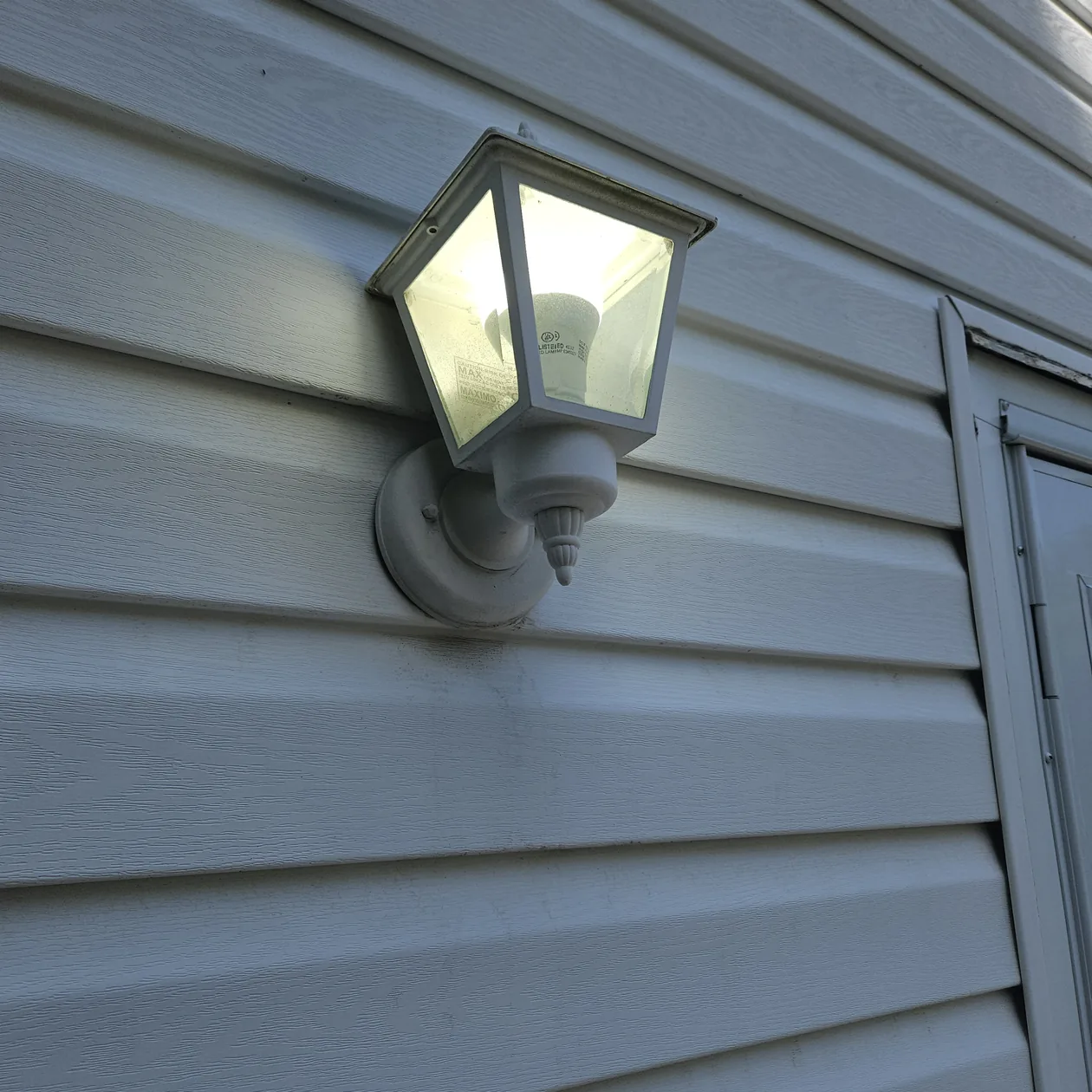 Exterior wall light mounted on pale siding beside a doorway.