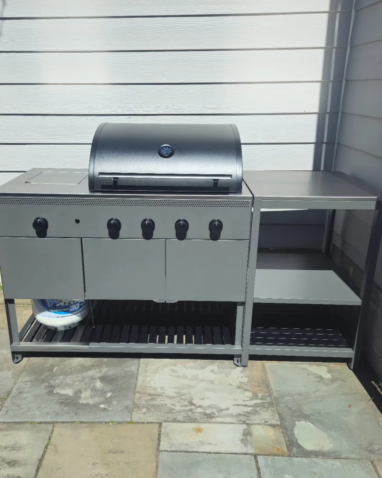 Freestanding outdoor grill with a side shelf on a stone patio.