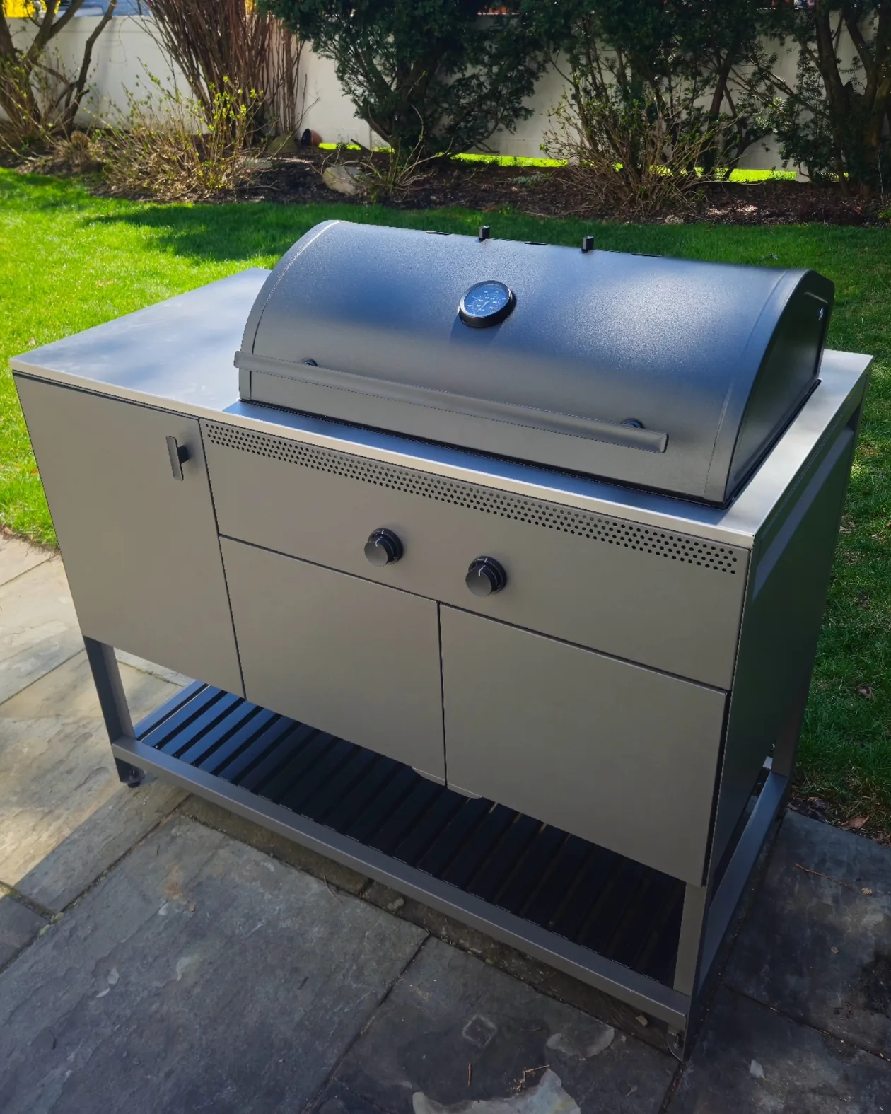 Freestanding outdoor grill on a stone patio beside a lawn.